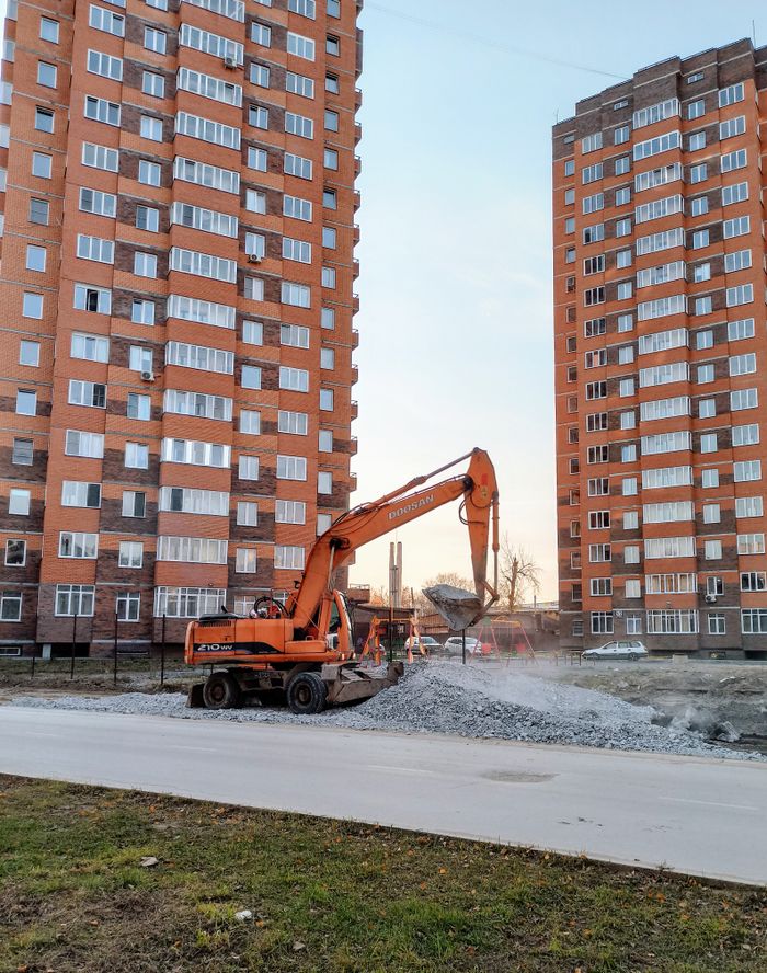 Excavator at construction site between residential buildings in Berdsk, Russia.